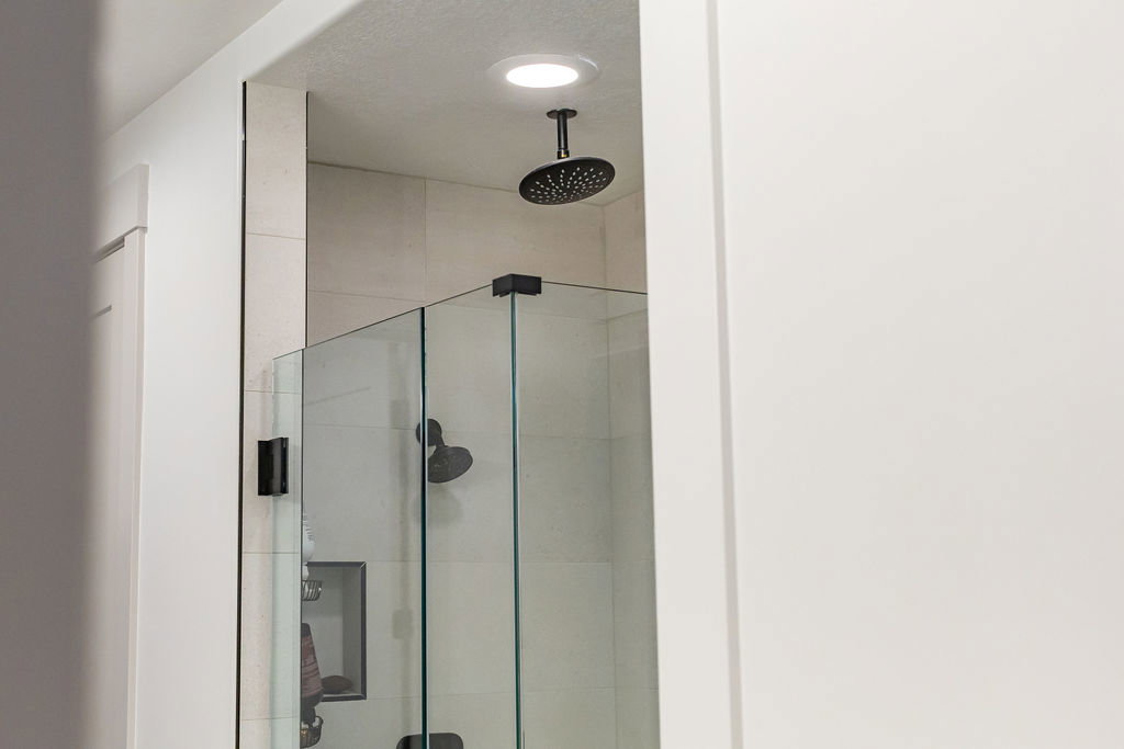 Frameless glass shower enclosure featuring a ceiling-mounted matte black rain shower head, large format tile surround, and a recessed shower niche