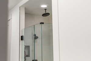 Frameless glass shower enclosure featuring a ceiling-mounted matte black rain shower head, large format tile surround, and a recessed shower niche