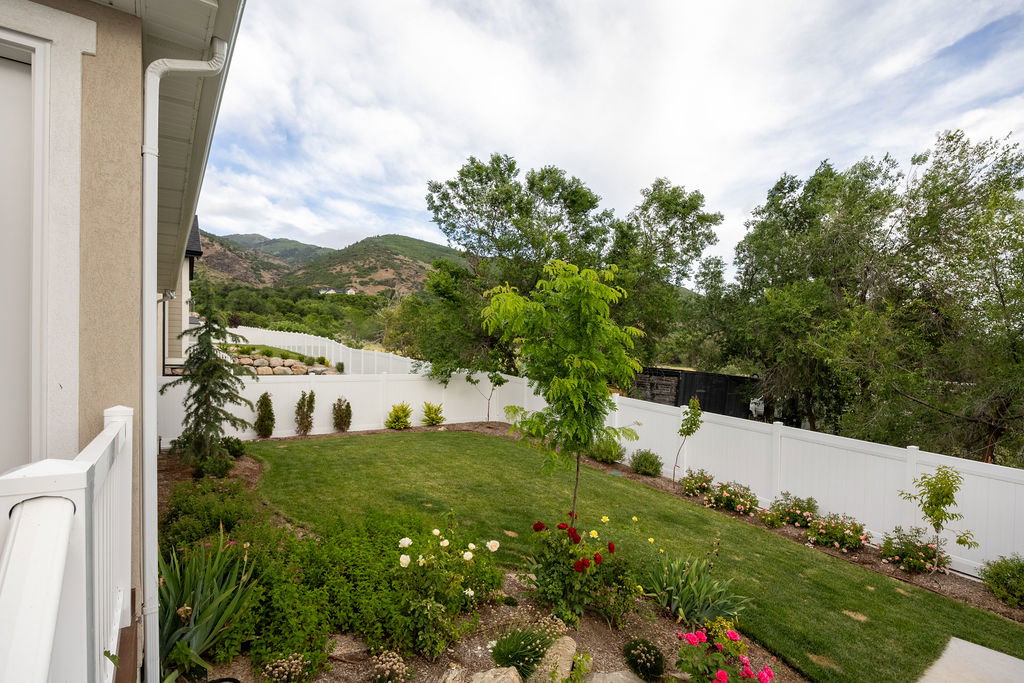 Expansive backyard featuring a manicured lawn, established landscaping, and a white privacy fence