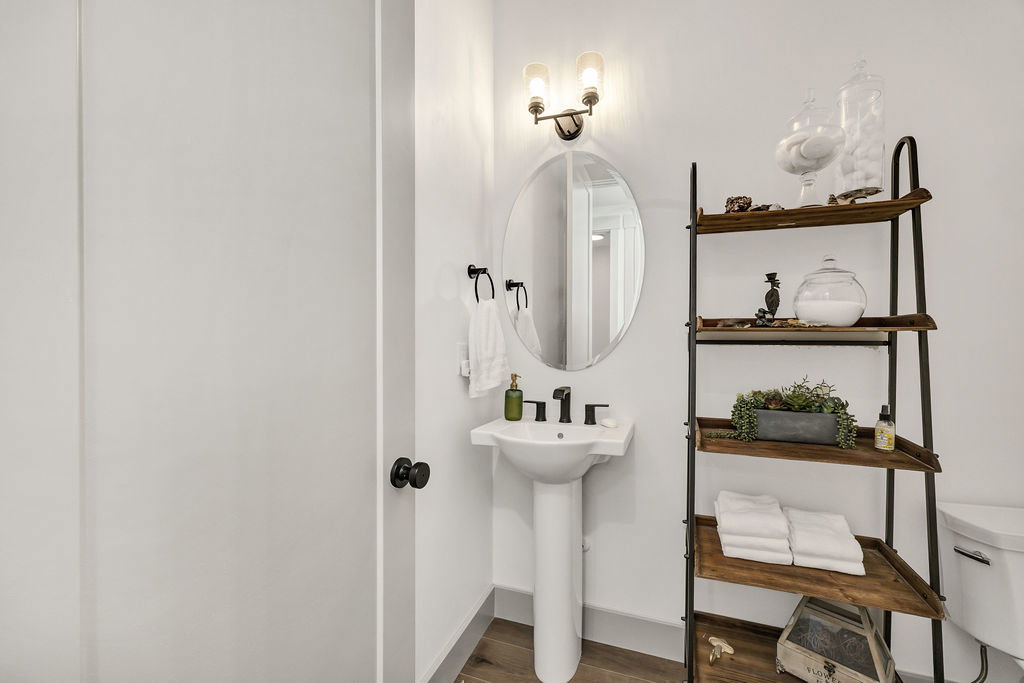 Pedestal sink with black faucet, an oval mirror, and a two-light vanity fixture