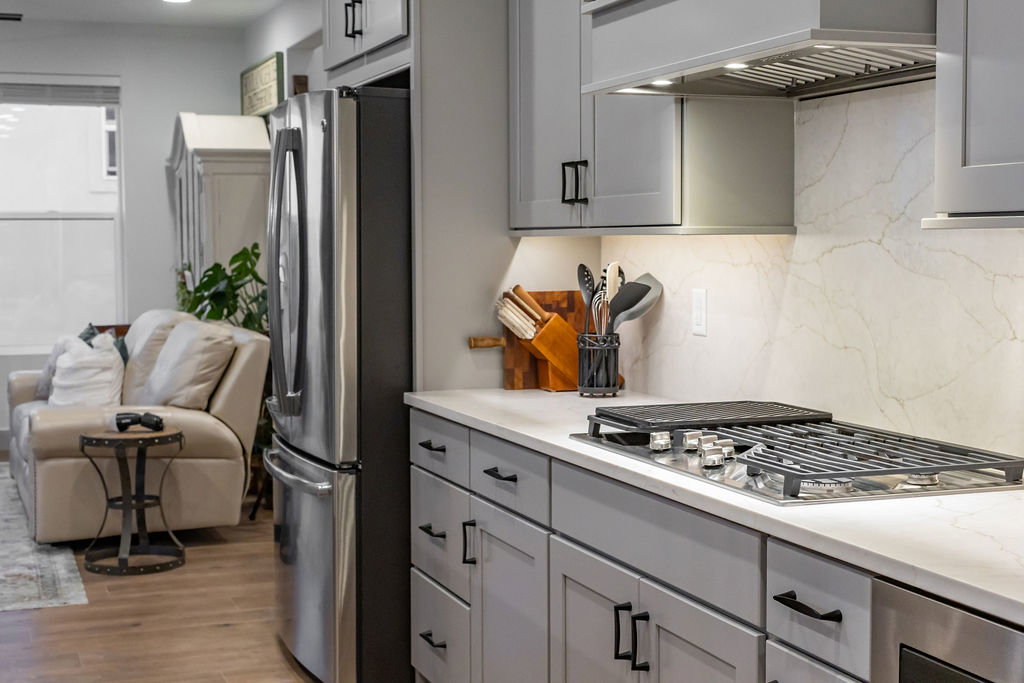 Kitchen featuring light gray cabinetry with black hardware, stainless steel refrigerator, and integrated gas cooktop with griddle