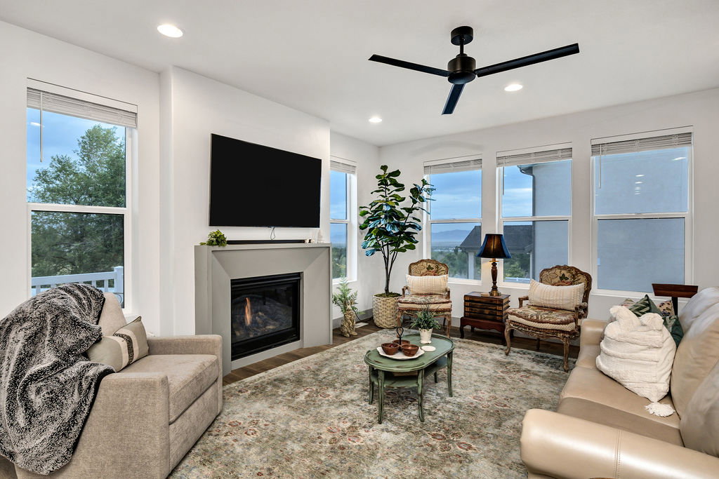 Living area featuring a modern fireplace with a light gray surround, multiple large windows, recessed lighting, and a contemporary black ceiling fan