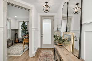 Foyer featuring wood-finish flooring, wainscoting, and a grey-framed entry door with frosted glass