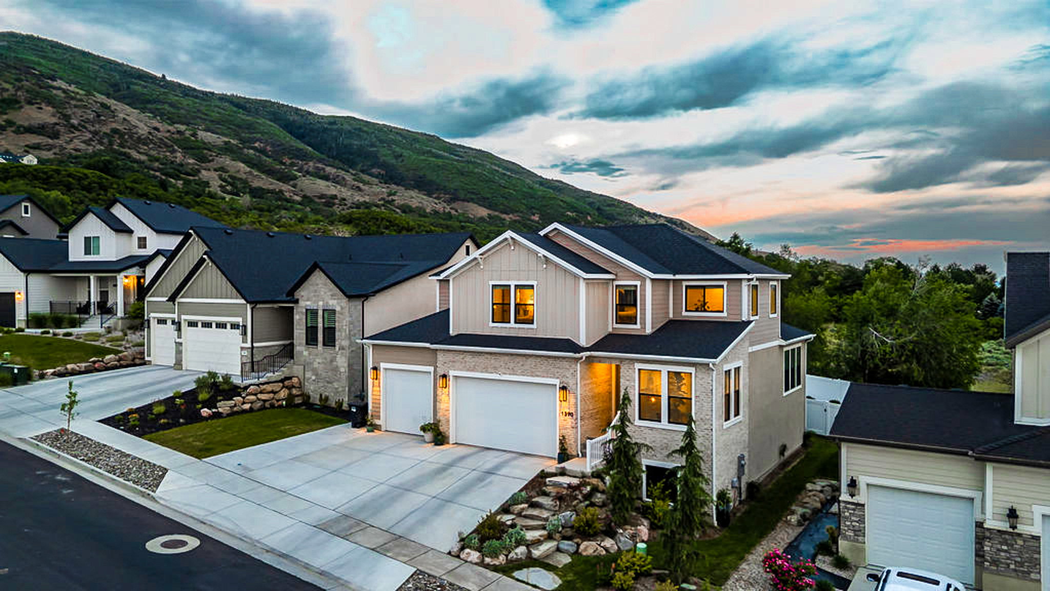 Contemporary architectural style with a stone and siding facade, featuring a two-car garage, established landscaping, and a mountain backdrop