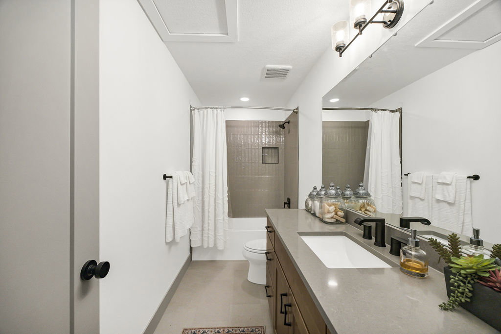 Bathroom featuring a large vanity with an integrated sink and matte black fixtures, a full-width mirror, tile flooring, and a bathtub with tiled surround and shower niche