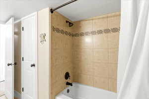 Bathtub and shower combination featuring beige tile surround with decorative accent band, dark bronze fixtures, and an adjacent linen closet with bi-fold doors