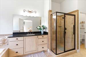 Bathroom featuring a large vanity with a dark countertop and undermount sink, an expansive mirror, and a glass-enclosed shower with tile surround