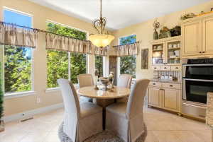 Expansive window array surrounding a dining area with a circular pedestal table, complemented by built-in cabinetry featuring glass display doors and a double wall oven