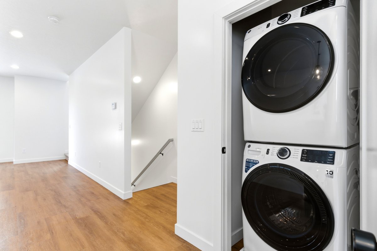 Dedicated laundry closet with stacked washer and dryer, wood-finish flooring, recessed lighting, and a modern stair railing