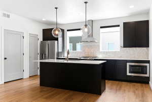 Modern kitchen featuring a central island with a light-colored countertop, dark cabinetry, stainless steel appliances, and wood-finish flooring
