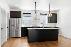 Modern kitchen featuring a central island, stainless steel appliances, black cabinetry, white countertops, and wood-finish flooring