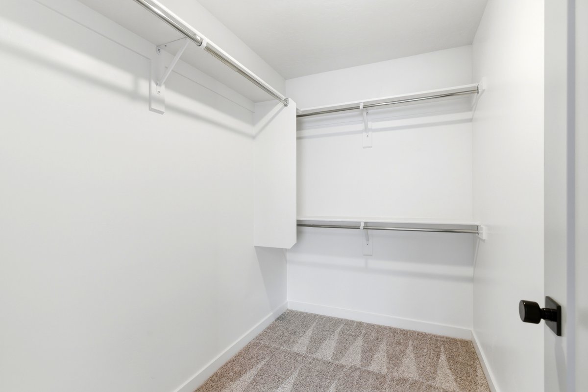 Walk-in closet featuring white walls, light-toned patterned carpet, and multiple built-in shelving units with hanging rods