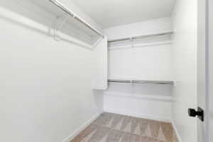 Walk-in closet featuring white walls, light-toned patterned carpet, and multiple built-in shelving units with hanging rods