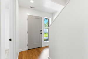 Entryway featuring wood-finish flooring, a contemporary light gray door with black hardware, and an adjacent sidelight window