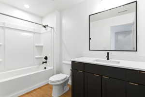 Bathroom featuring a white tub/shower combination with black fixtures, a white toilet, and wood-finish flooring