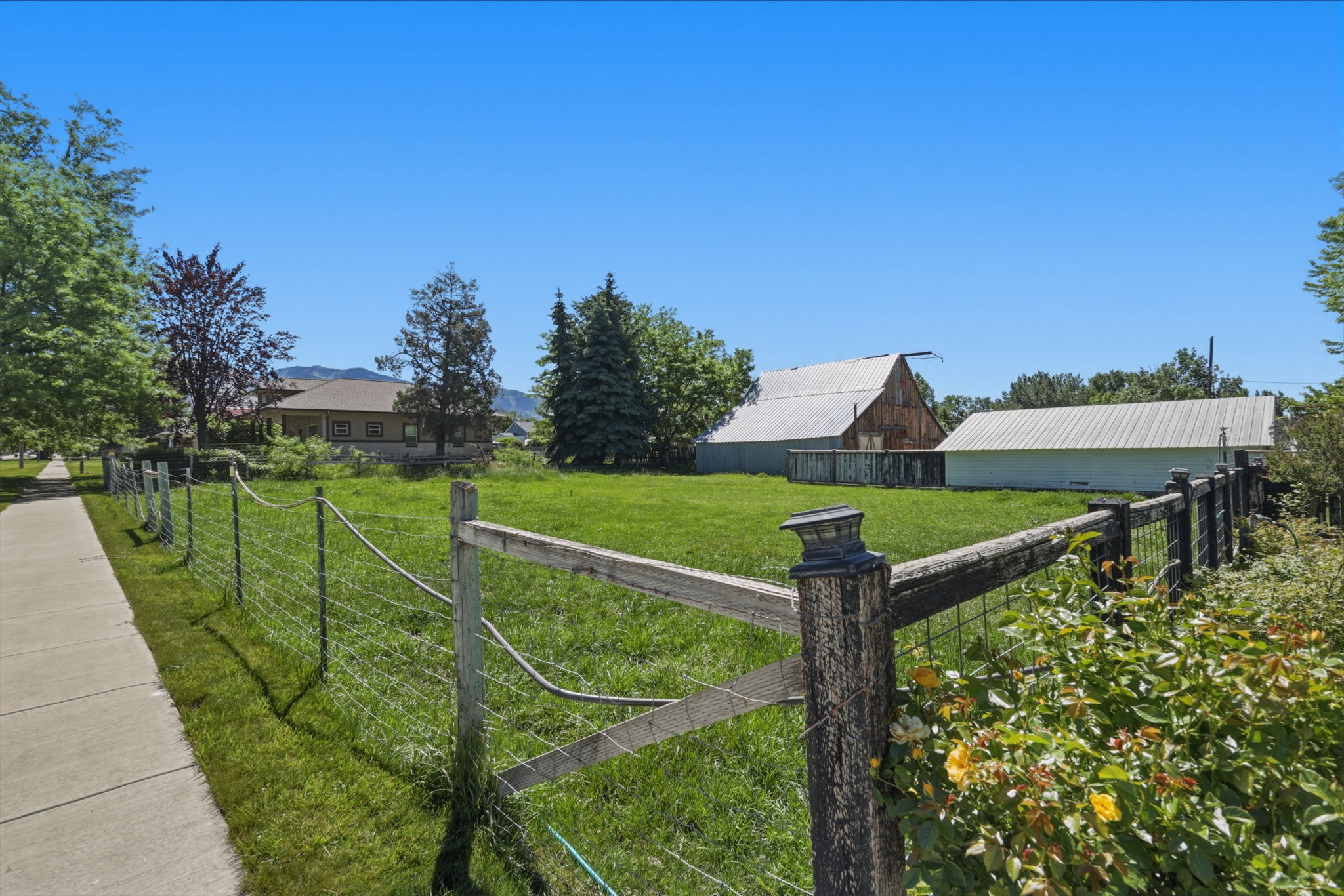 Expansive green space featuring a wire and wood-post fence, mature trees, and distant outbuildings