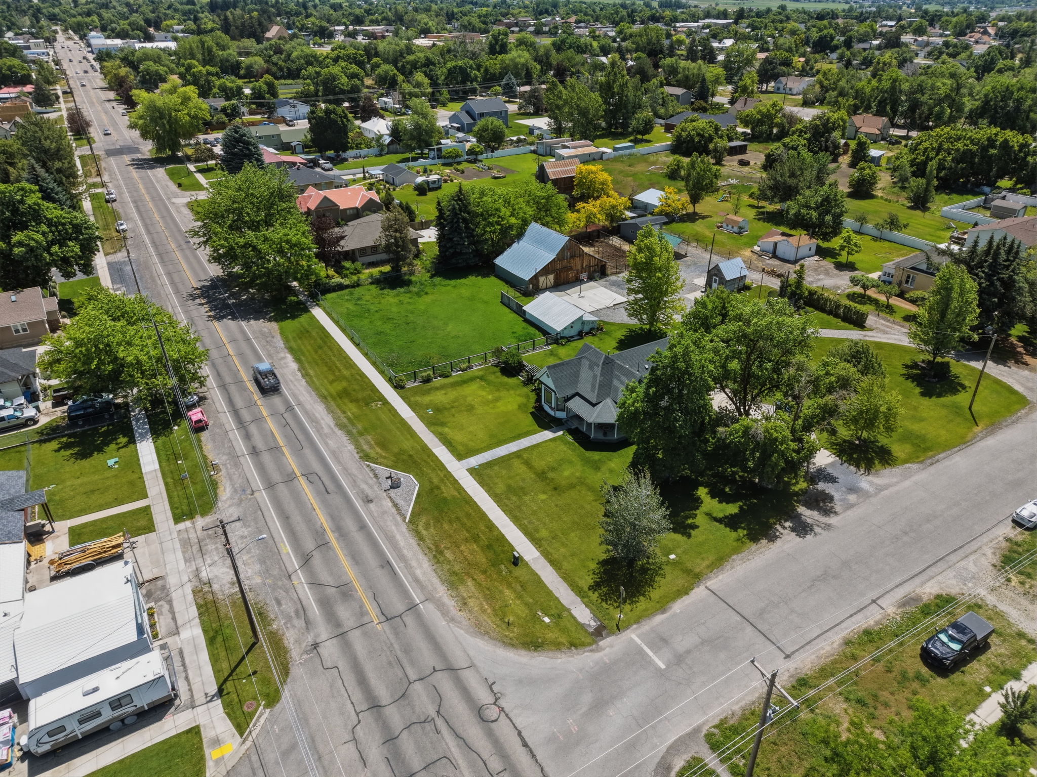 Aerial perspective showcasing a corner property with mature trees and a manicured lawn