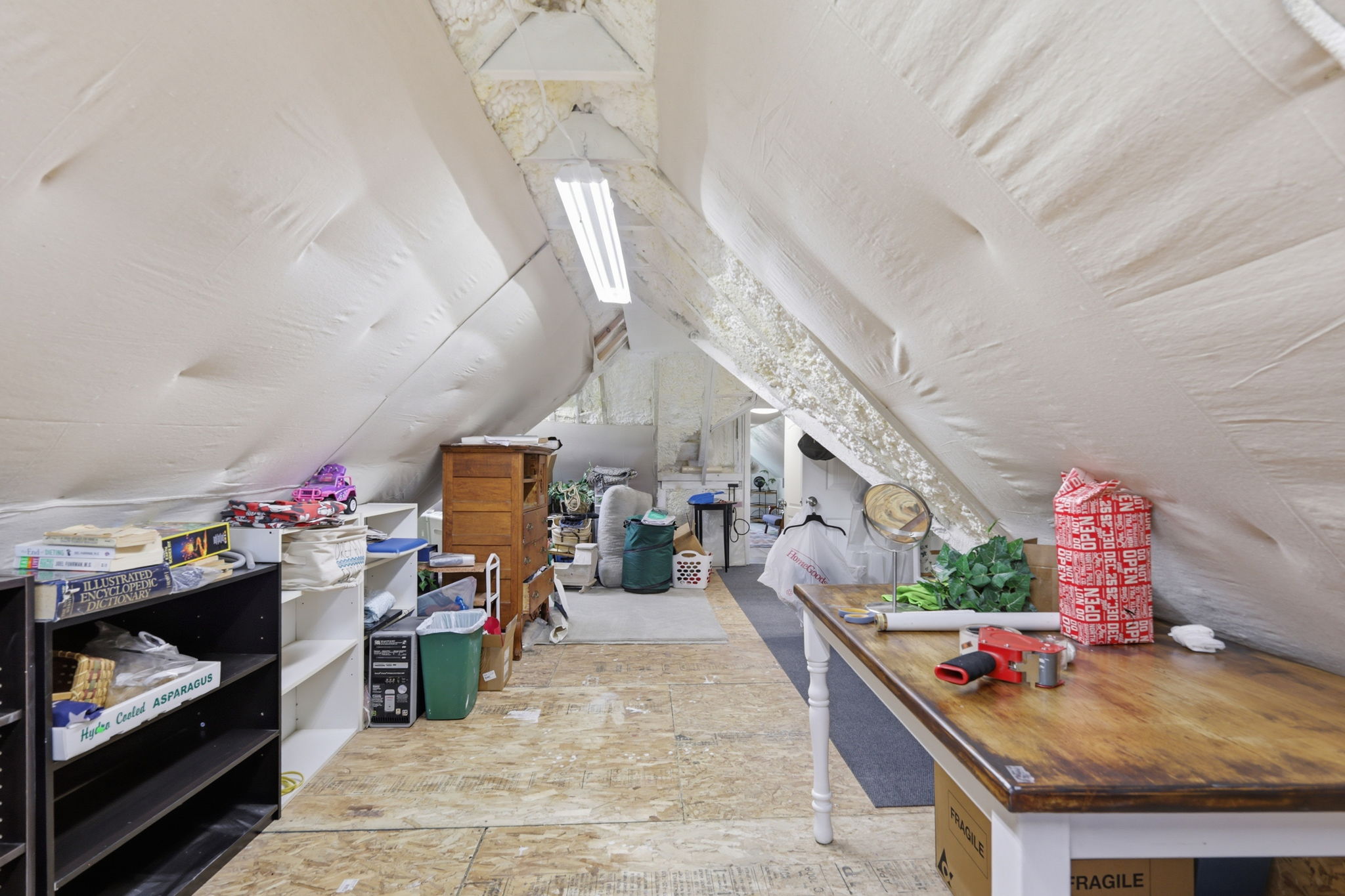 Attic space featuring sloped, insulated walls, unfinished wood-finish flooring, and fluorescent lighting fixtures