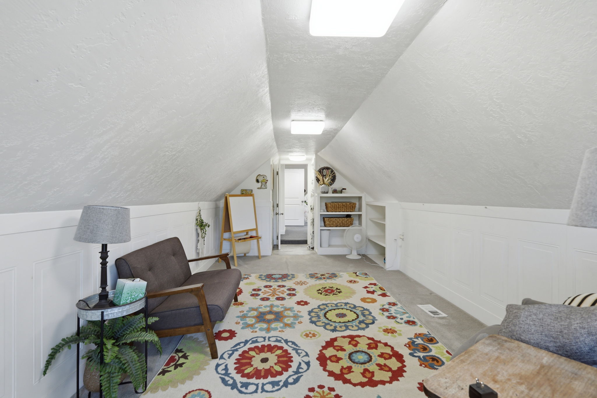Attic space featuring sloped ceilings, recessed lighting, white paneled wainscoting, and built-in shelving units
