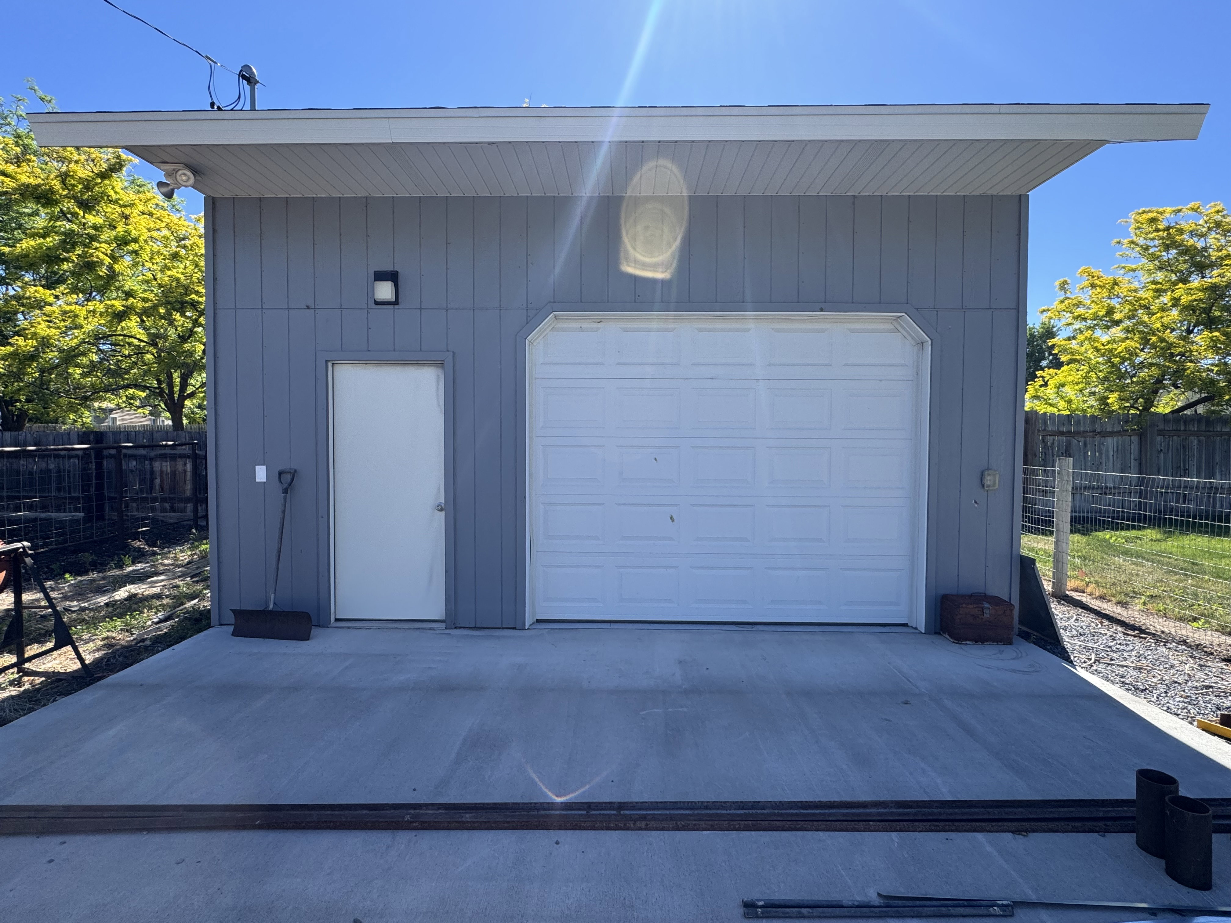 Detached structure featuring vertical panel siding, an overhead garage door, a pedestrian entry door, a deep eave overhang, and concrete flatwork