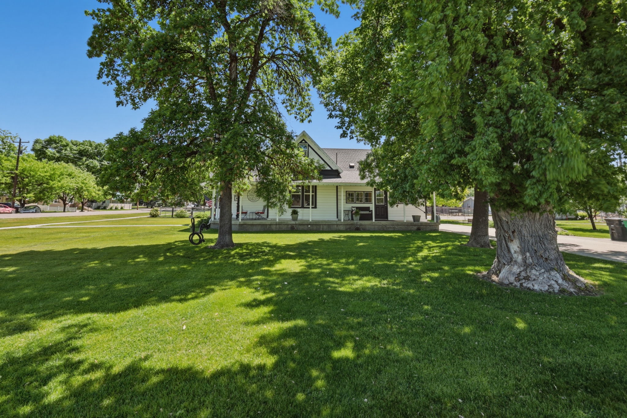 Expansive front yard featuring a manicured lawn, mature shade trees, and a white exterior home with a covered front porch