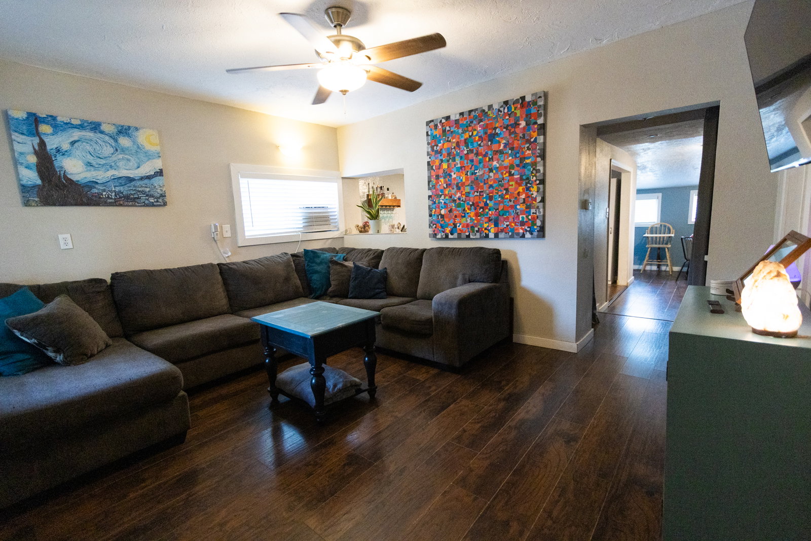 Living area featuring dark wood-finish flooring, light neutral walls, and a ceiling fan with integrated lighting