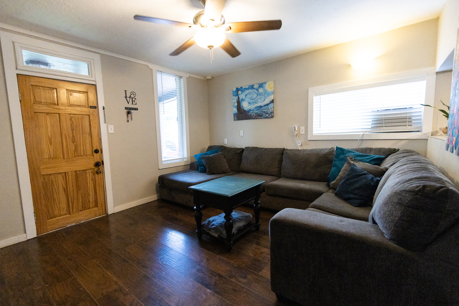 Living area featuring wood-finish flooring, a wood paneled entry door with transom window, and a ceiling fan with light fixture
