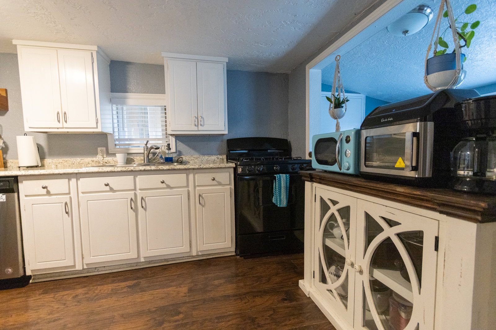 Kitchen with wood-finish flooring, white cabinetry, a built-in dishwasher, and a black range