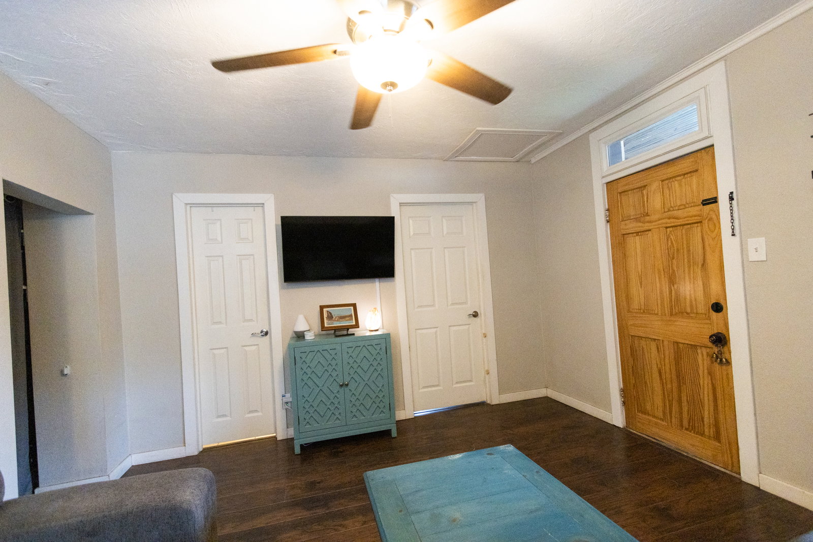 Interior room featuring wood-finish flooring, a natural wood paneled door with transom window, and a ceiling fan with integrated lighting