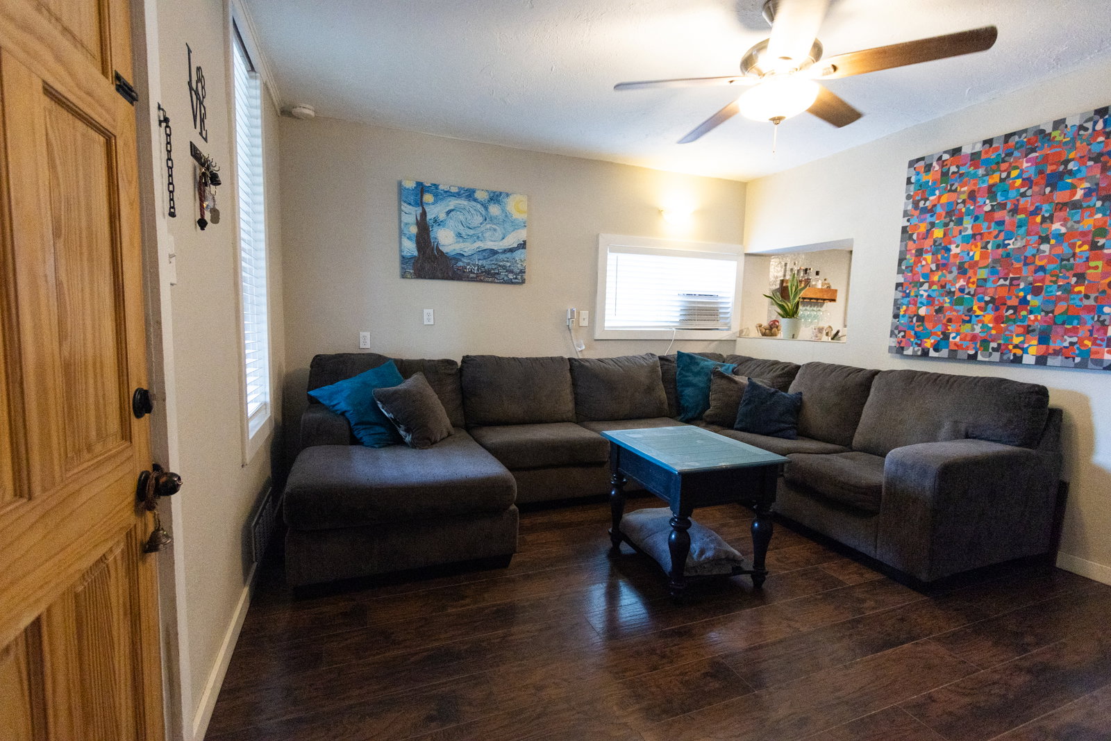 Living area featuring dark wood-finish flooring, neutral wall paint, and a ceiling fan with integrated lighting