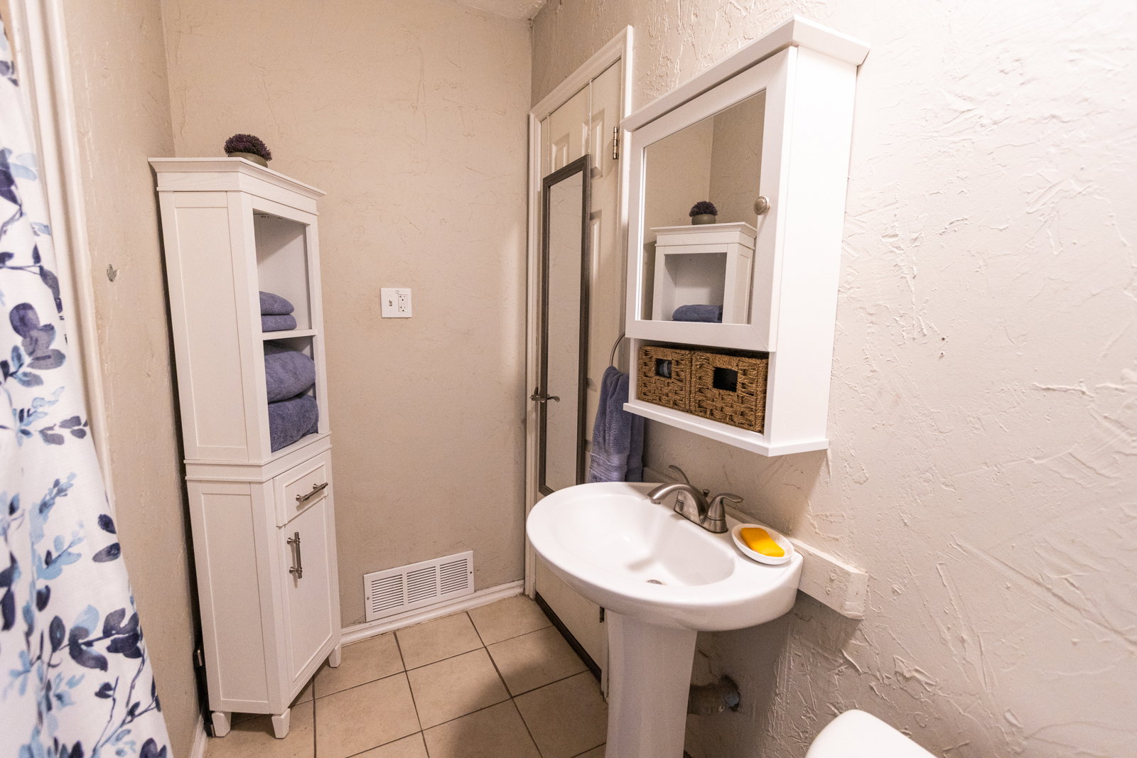 Pedestal sink with chrome hardware, complemented by a mirrored medicine cabinet featuring integrated shelving