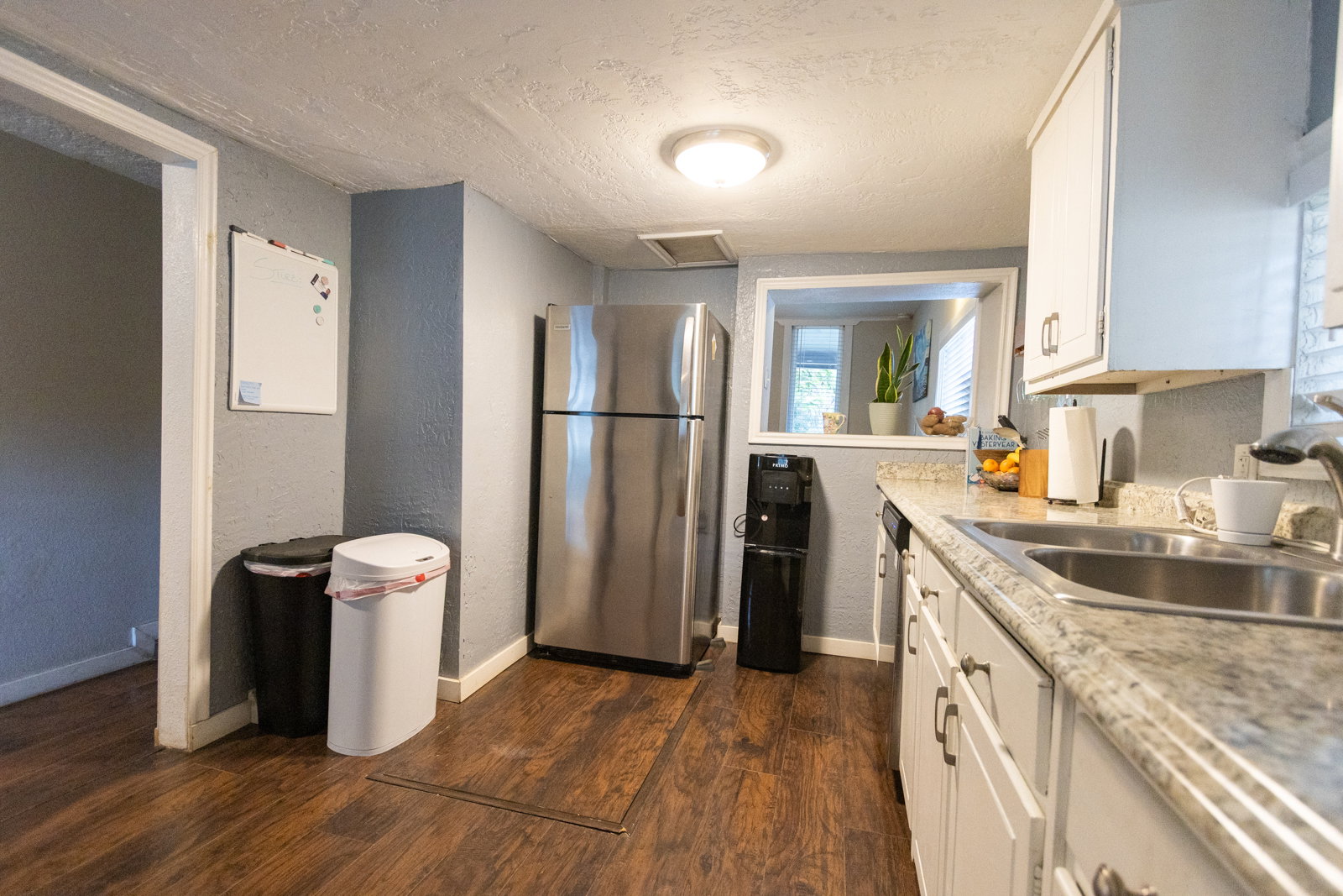 Kitchen featuring wood-finish flooring, stainless steel refrigerator, white cabinetry, granite-style countertops, and a pass-through window