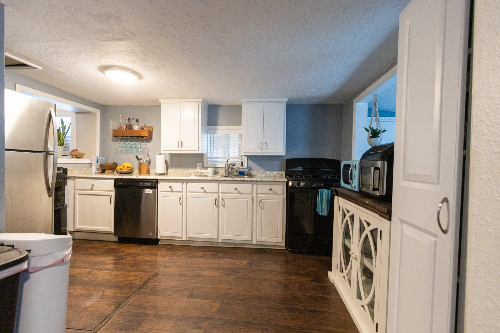 Kitchen featuring wood-finish flooring, white cabinetry, a stainless steel refrigerator, a black range, and light-toned countertops
