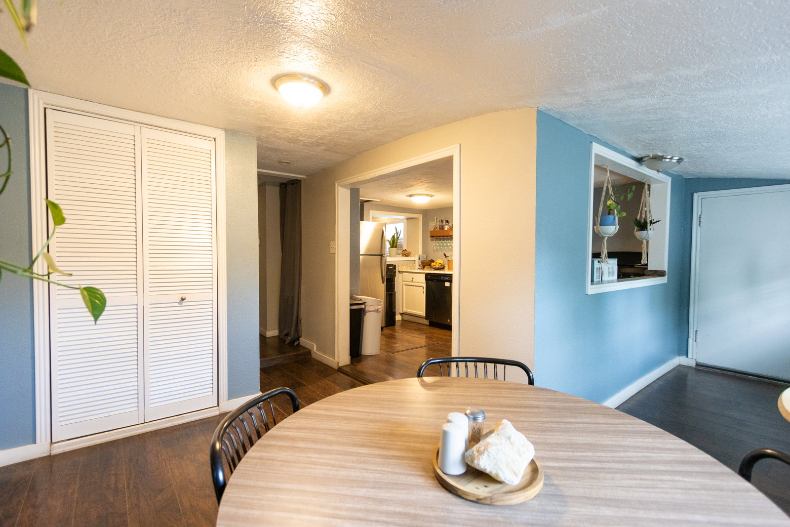 Wood-finish flooring throughout, featuring a kitchen pass-through window, white louvered bifold closet doors, and recessed ceiling lighting