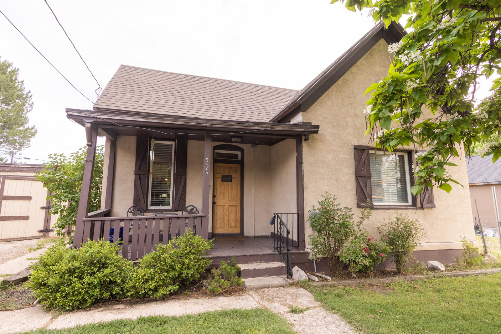 Stucco exterior featuring a covered front porch with dark railing, a light wood-finish entry door, and dark wood-finish shutters