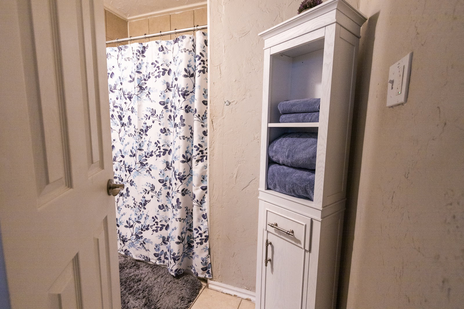 White storage cabinet featuring open shelving and a lower cabinet with brushed nickel hardware