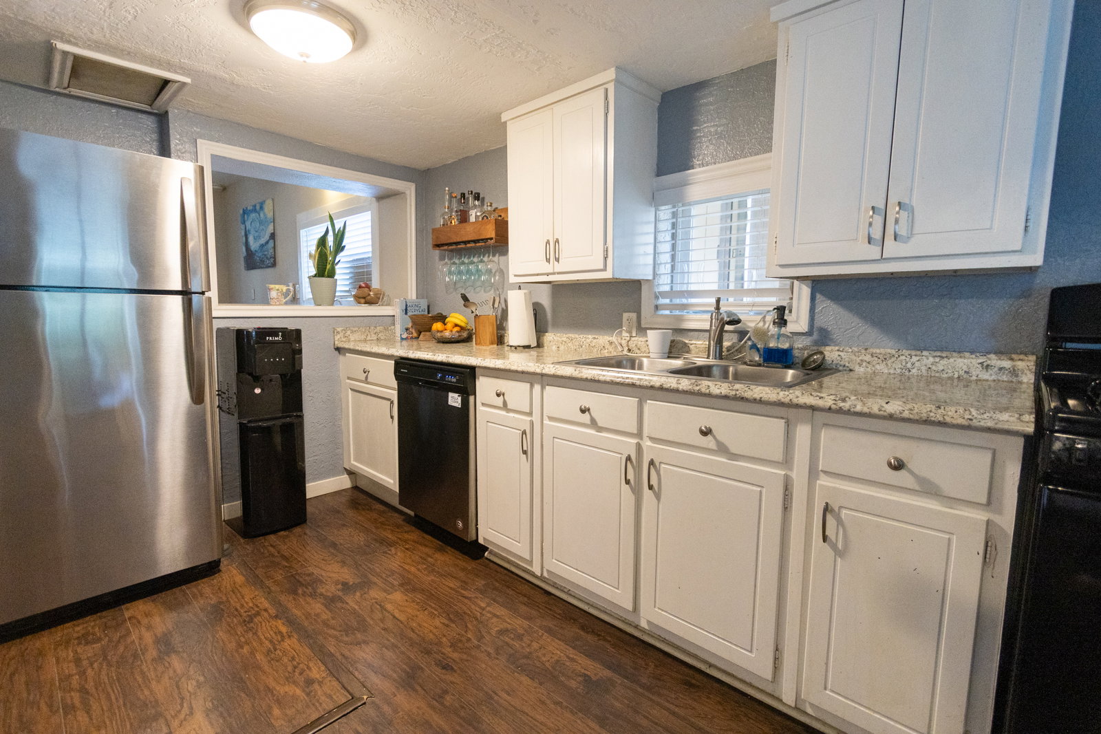 Kitchen featuring wood-finish flooring, white cabinetry, a double basin stainless steel sink, and light-toned countertops