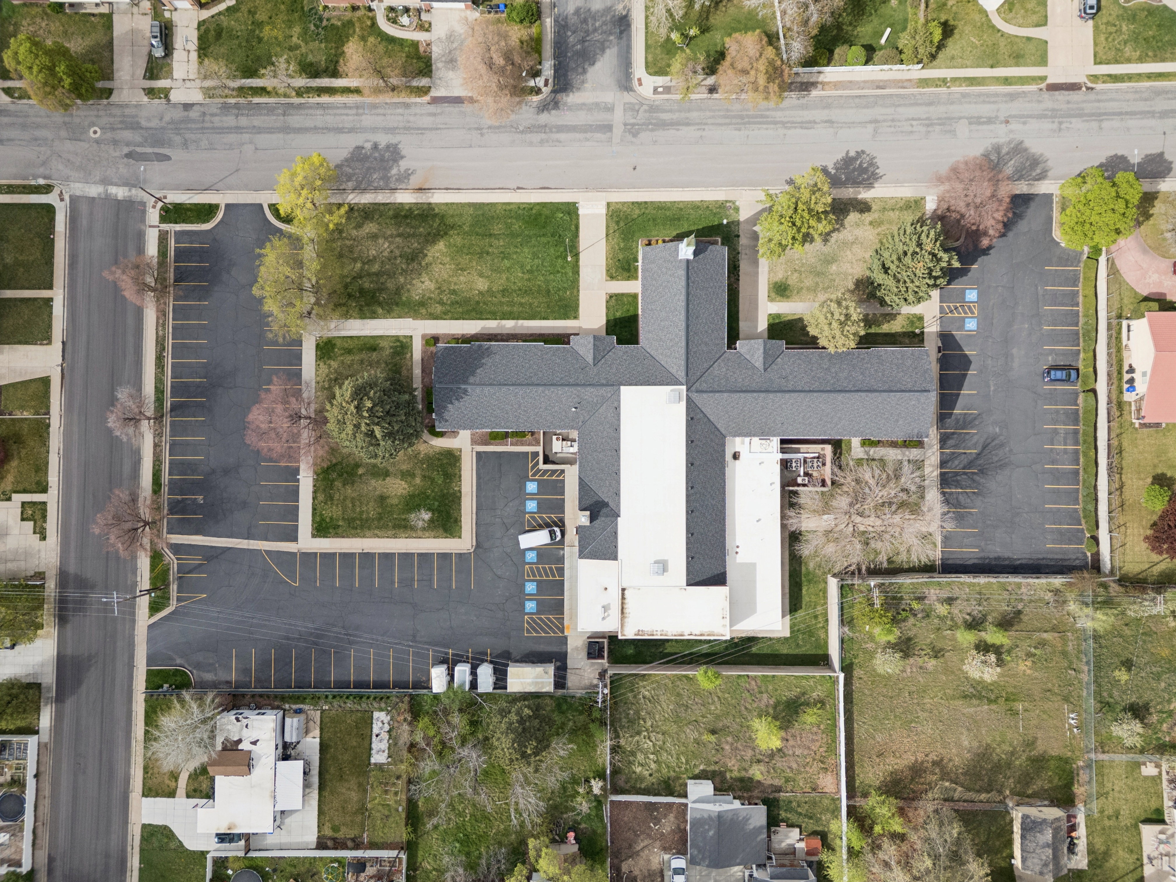 Aerial view of property with structure, paved parking lot with clearly marked stalls, and trees.