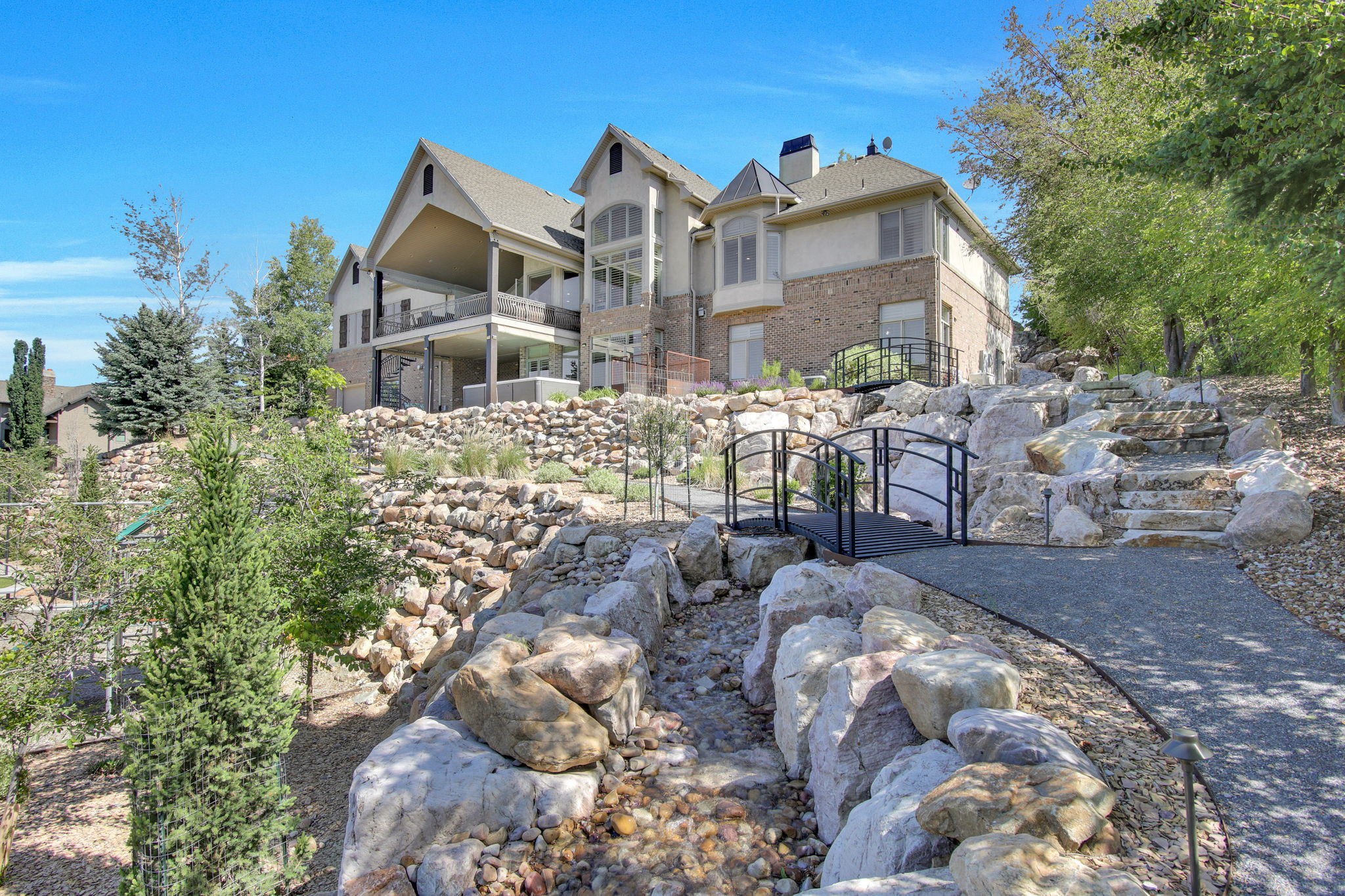 Expansive terraced yard featuring a rock garden, multiple bridges, a winding pathway, and mature trees