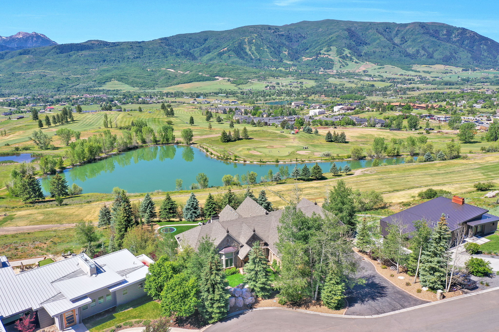 Aerial perspective highlighting the property with a dark shingle roof and multiple gables, situated in a landscaped setting with mature trees