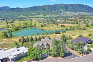 Aerial perspective highlighting the property with a dark shingle roof and multiple gables, situated in a landscaped setting with mature trees