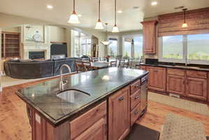 Kitchen island with an undermount sink and dark countertop, wood-finish flooring, wood cabinetry, recessed lighting, and expansive windows