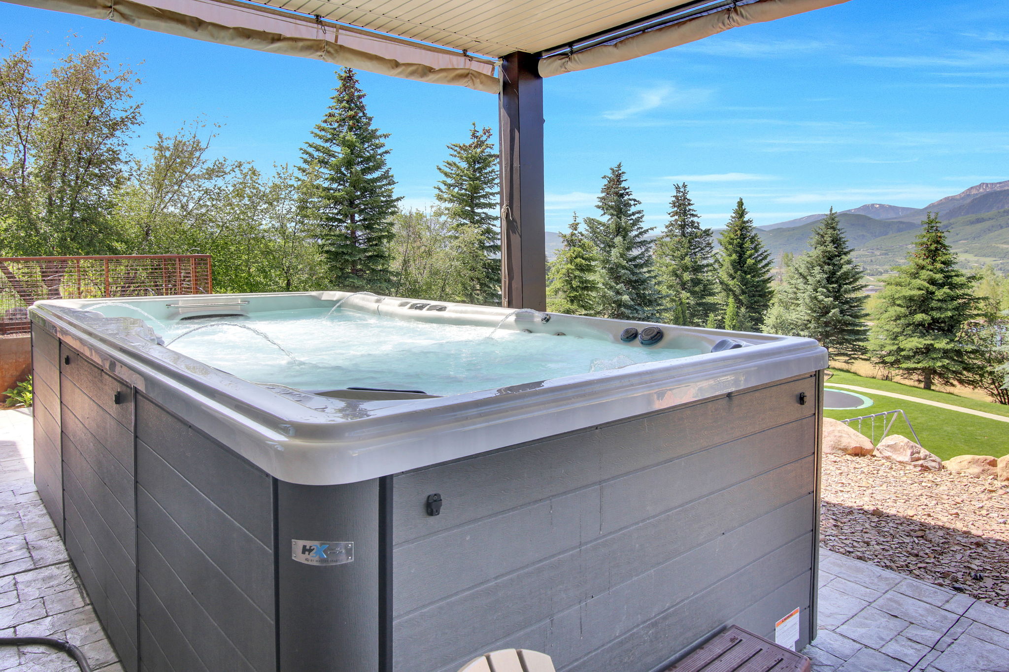 Outdoor hot tub situated on a stamped concrete patio, offering mountain scenery and surrounding mature trees