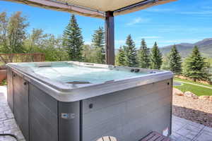 Outdoor hot tub situated on a stamped concrete patio, offering mountain scenery and surrounding mature trees