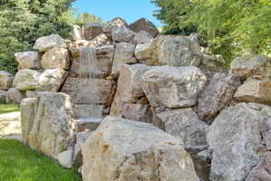 Custom rock waterfall feature with multi-tiered cascades, surrounded by natural boulders and verdant landscaping