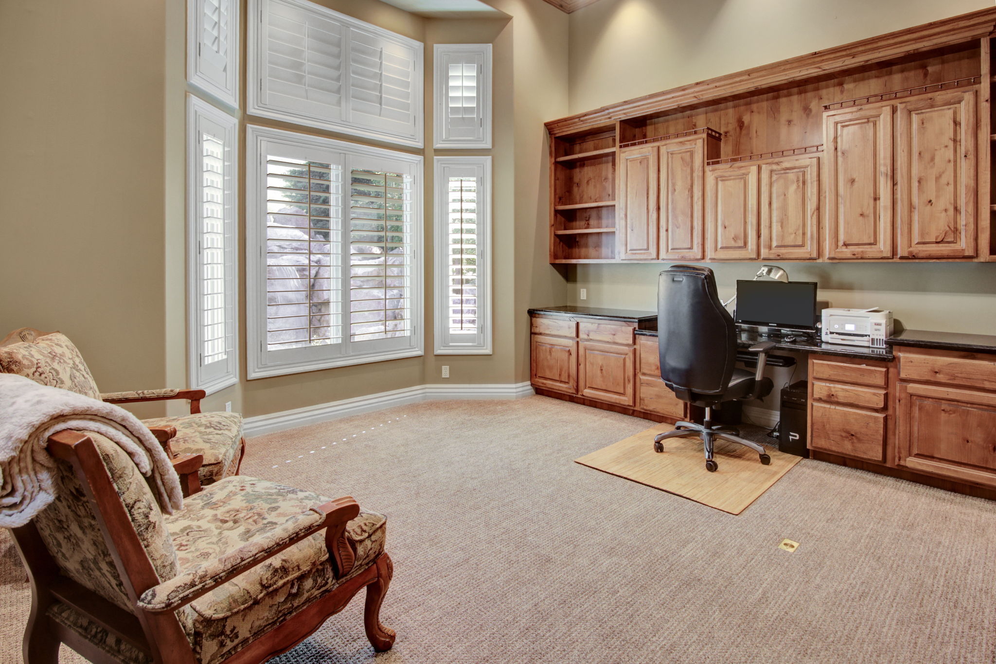 Spacious room featuring a built-in wood cabinetry system, dark countertops, and a bay window with white plantation shutters
