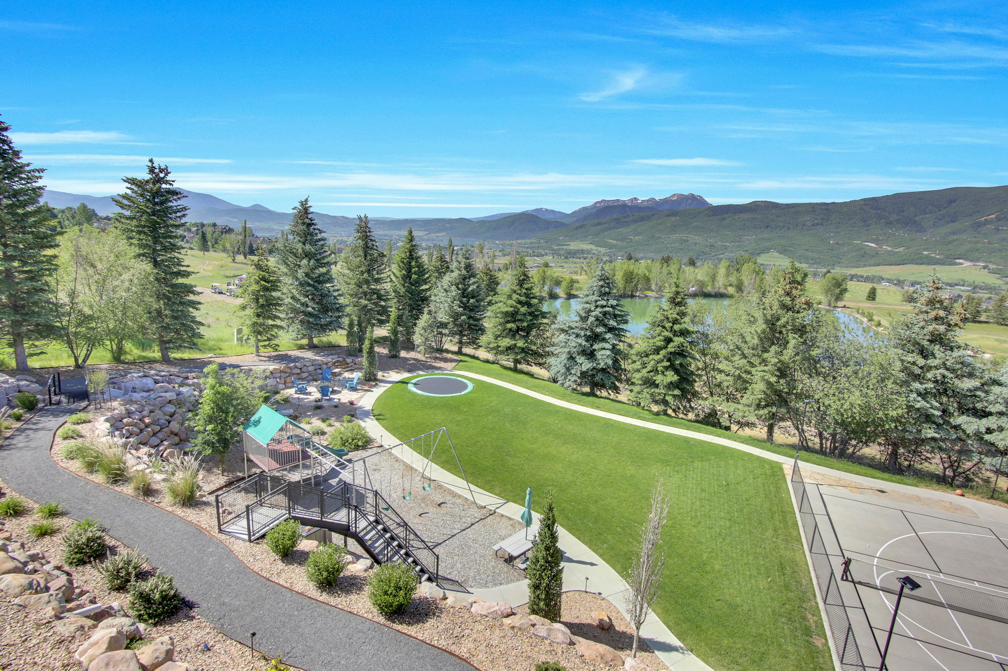 Expansive outdoor recreation area featuring a manicured lawn, dedicated playground, basketball court, and scenic water feature