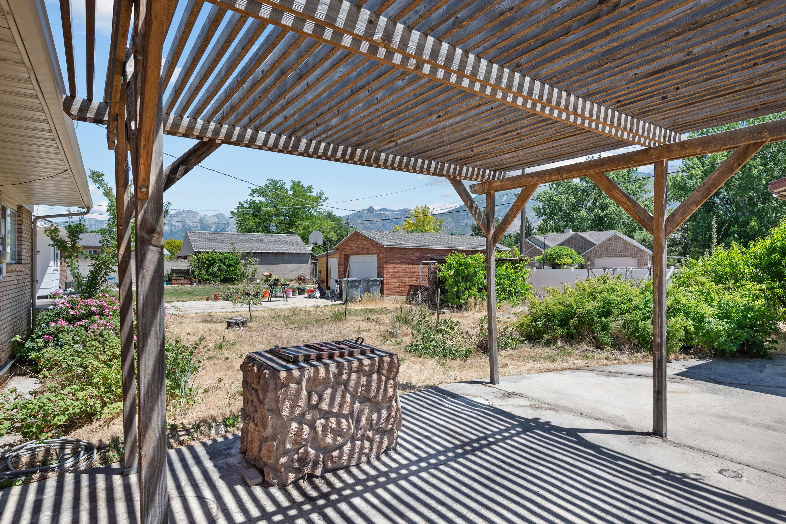 Wood pergola covering a paved patio with a built-in stone grill
