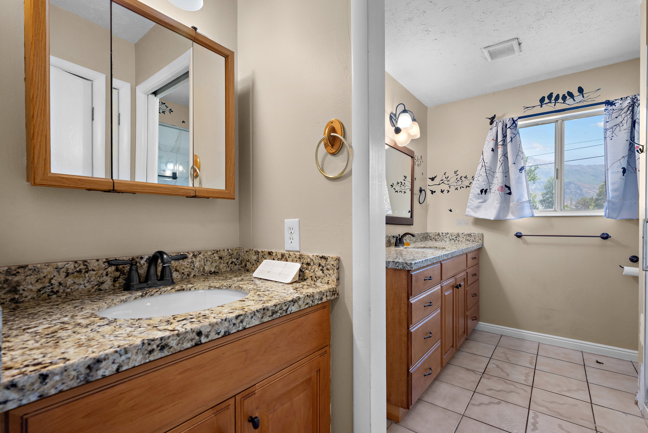 Double vanity bathroom featuring wood-finish cabinetry, granite-patterned countertops, and tile flooring