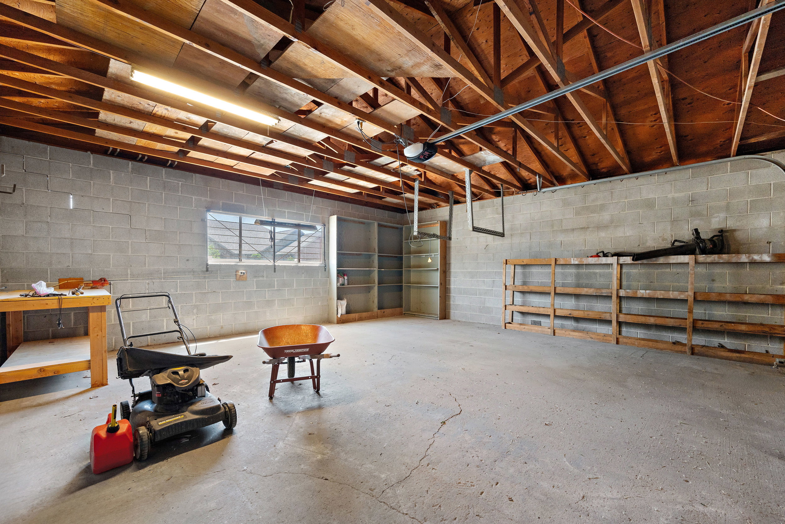 Spacious garage featuring exposed wood beam ceiling, concrete block walls, and a concrete floor